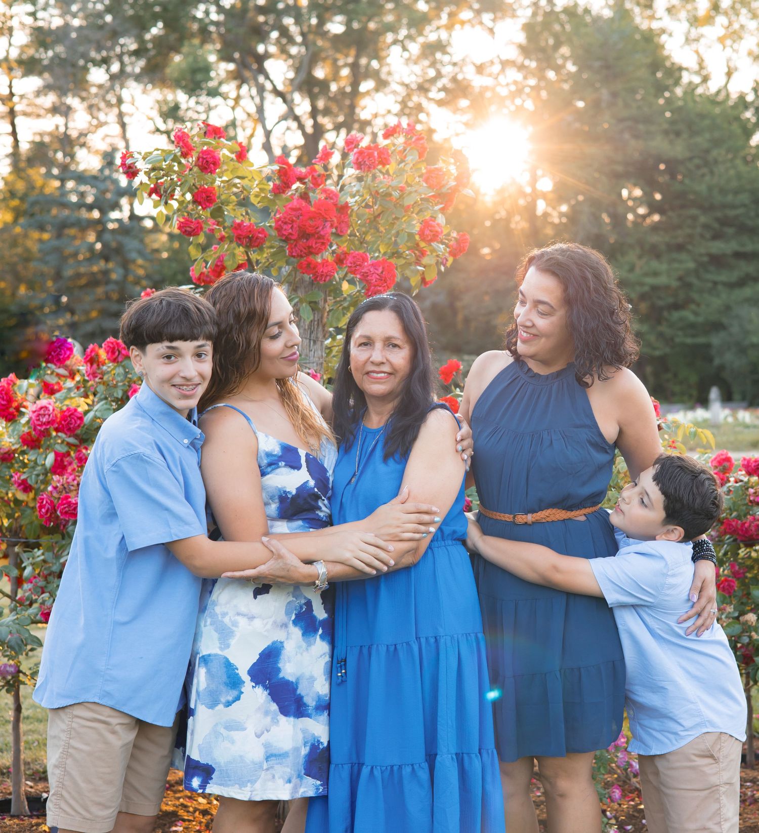 Group wearing coordinated blue outfits embracing by pink flowering bushes at sunset.