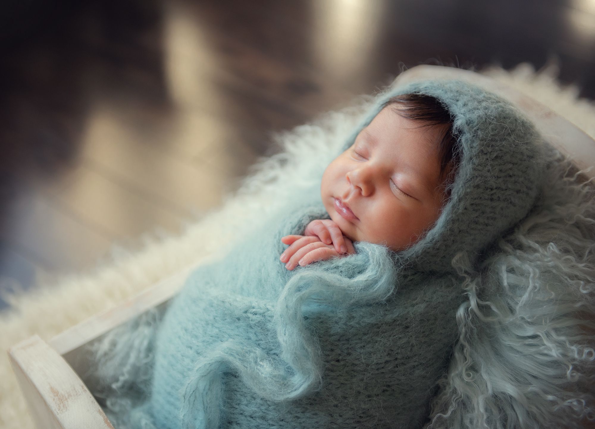 a baby boy in blue wrap and hat is in the crib prop posing for a newborn photo session at home in Kleinburg