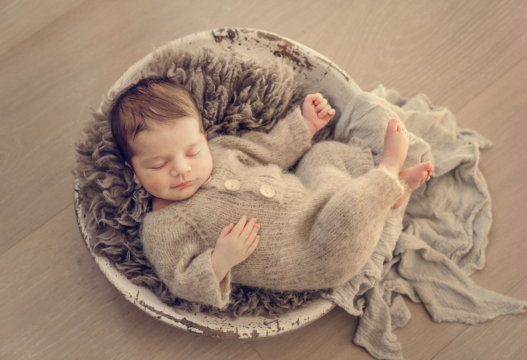 Sleeping baby swaddled in soft gray blanket lying on textured backdrop in vintage-style newborn photography series.
