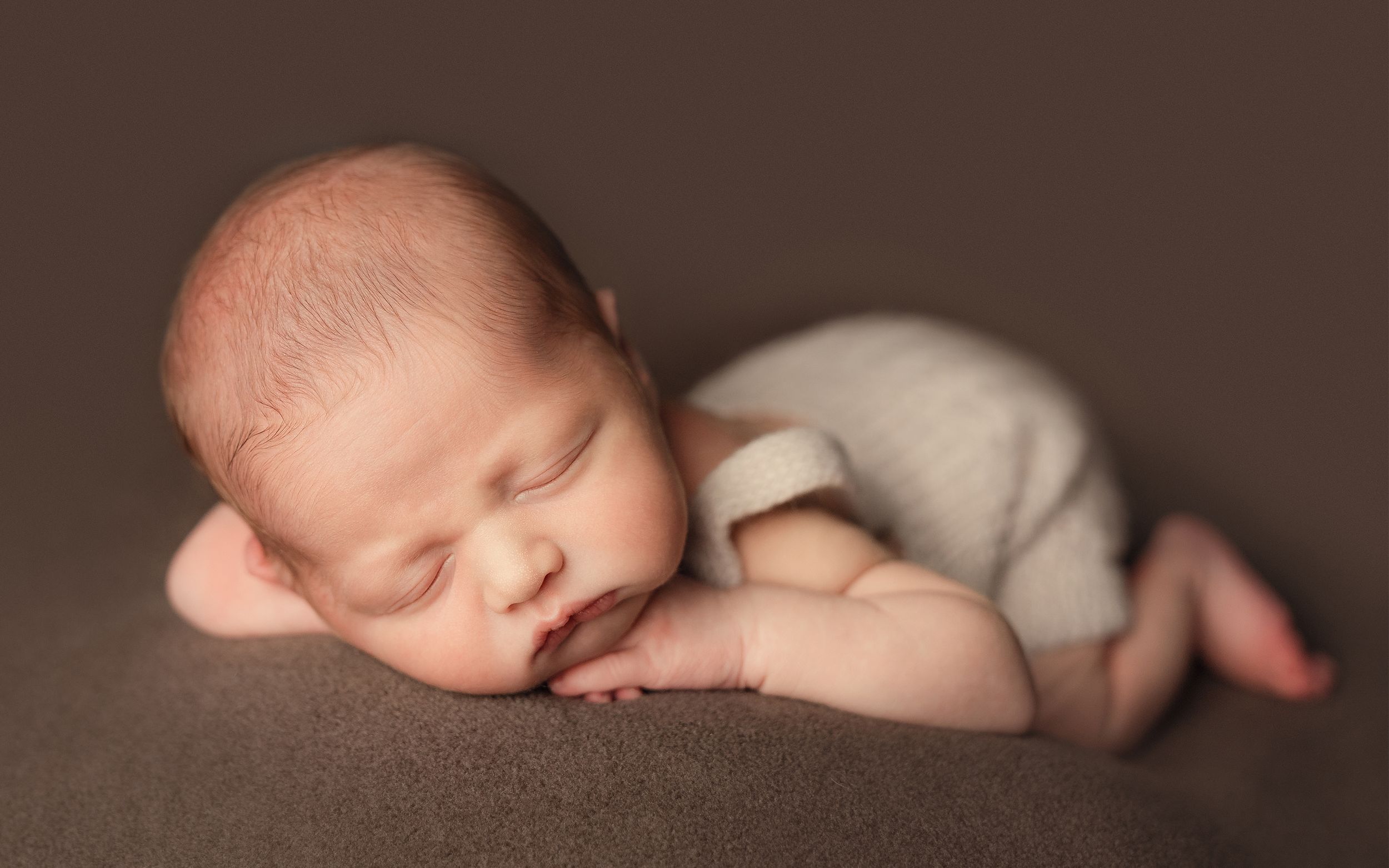 A series of artistic newborn photography shots showing a sleeping baby on brown fabric in different poses.