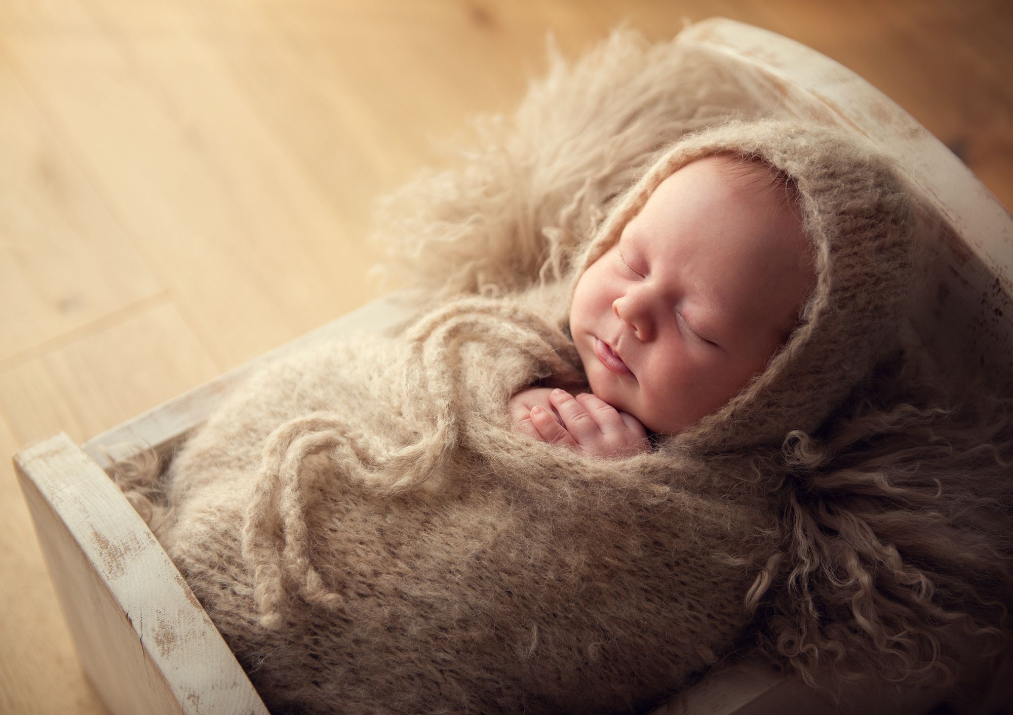 newborn baby is sleeping in a crib prop during the newborn photo session at home all wrapped in a cozy alpaca fur