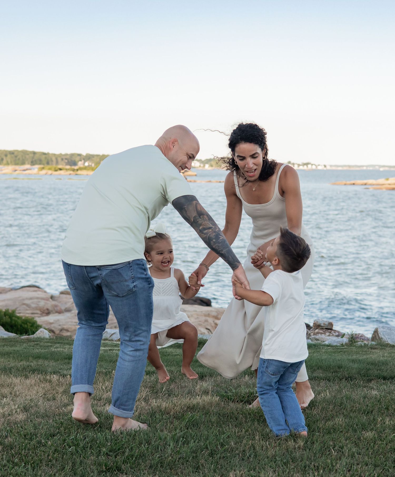 Family playfully dancing and having fun together on grassy hill by the ocean.