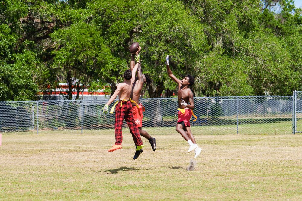 Young athletes jumping to catch a football during an outdoor flag football game on a grassy field in Tampa.