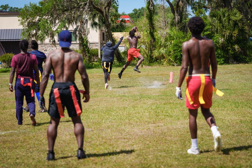 Group of young men playing flag football on a sunny outdoor field surrounded by palm trees in Tampa.