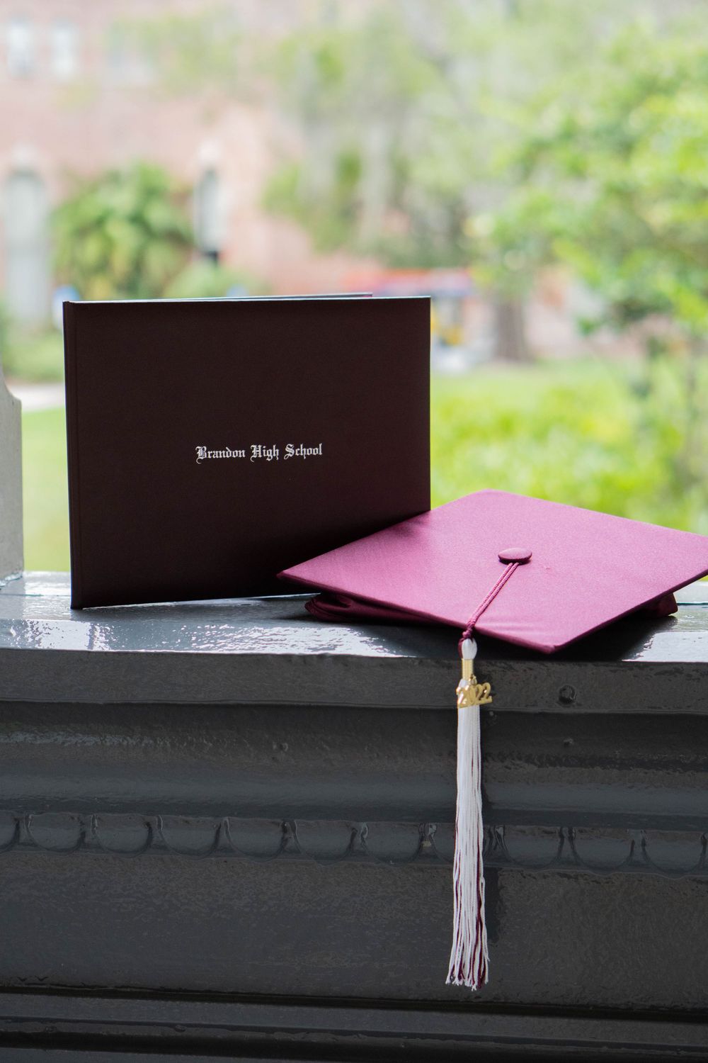 Brandon High School maroon graduation cap and diploma cover displayed on a windowsill with greenery behind in Tampa.