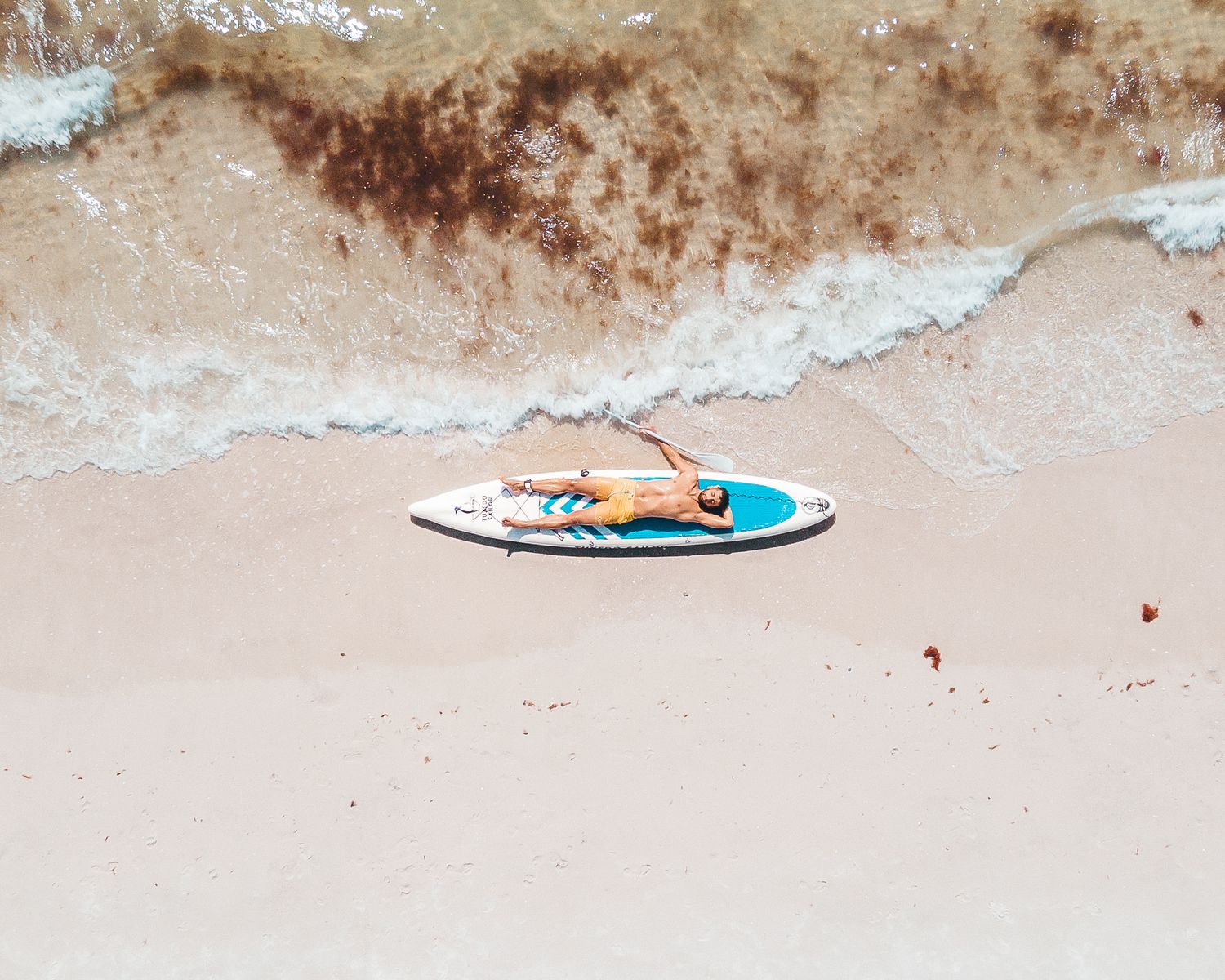 Orange inflatable surfboard floating on shallow ocean waves near sandy beach.