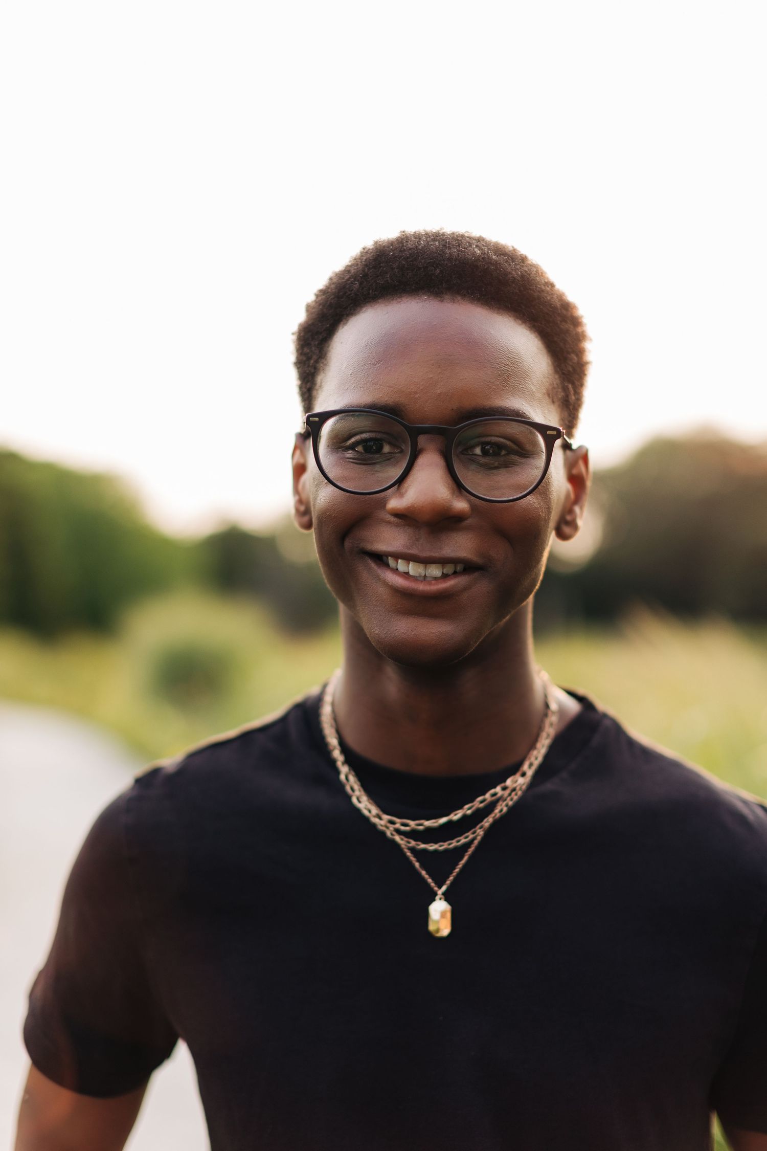 Close-up outdoor portrait featuring glasses and layered gold necklaces against natural lighting.