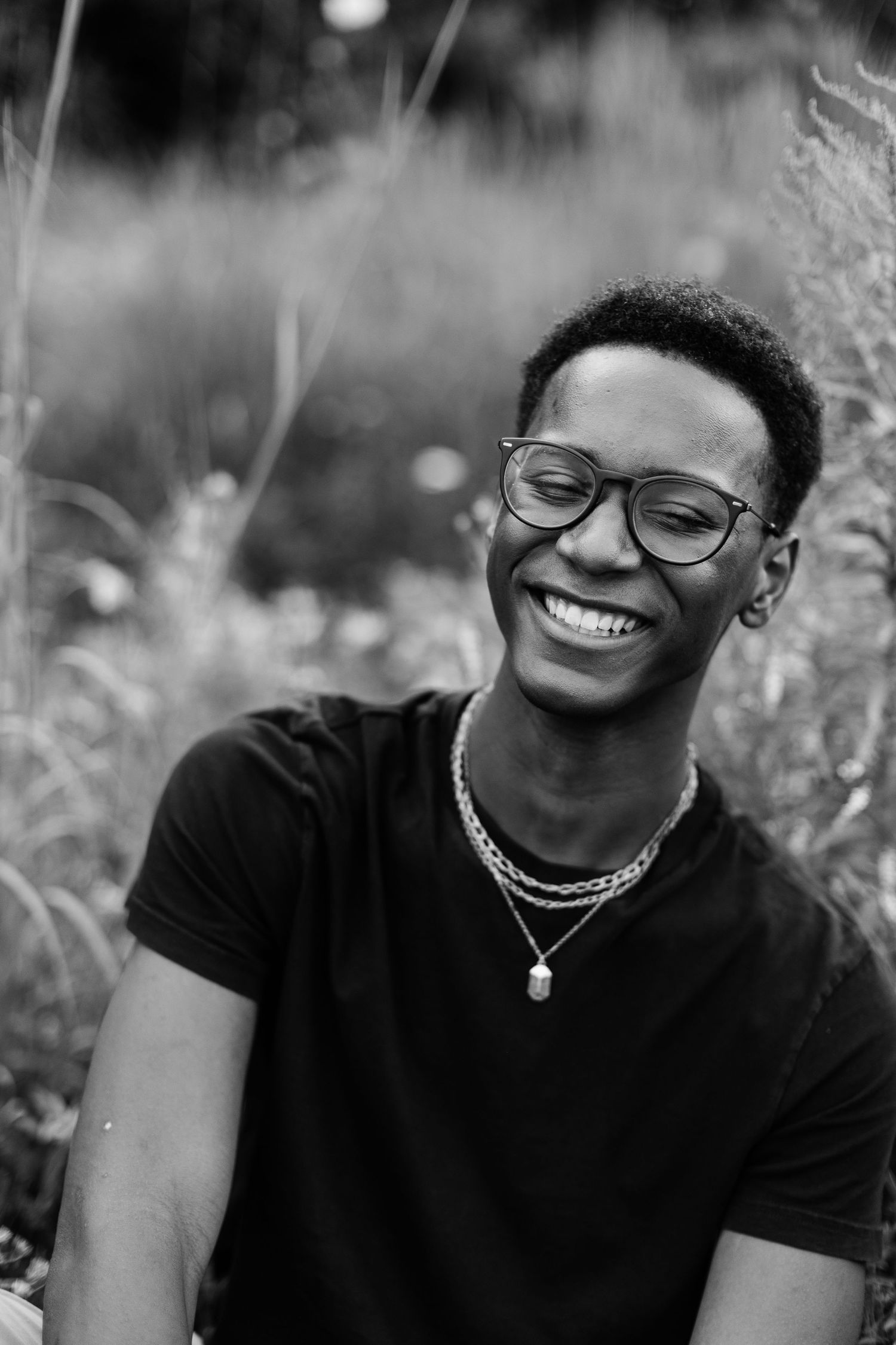 Black and white portrait showing joyful expression with glasses and jewelry.