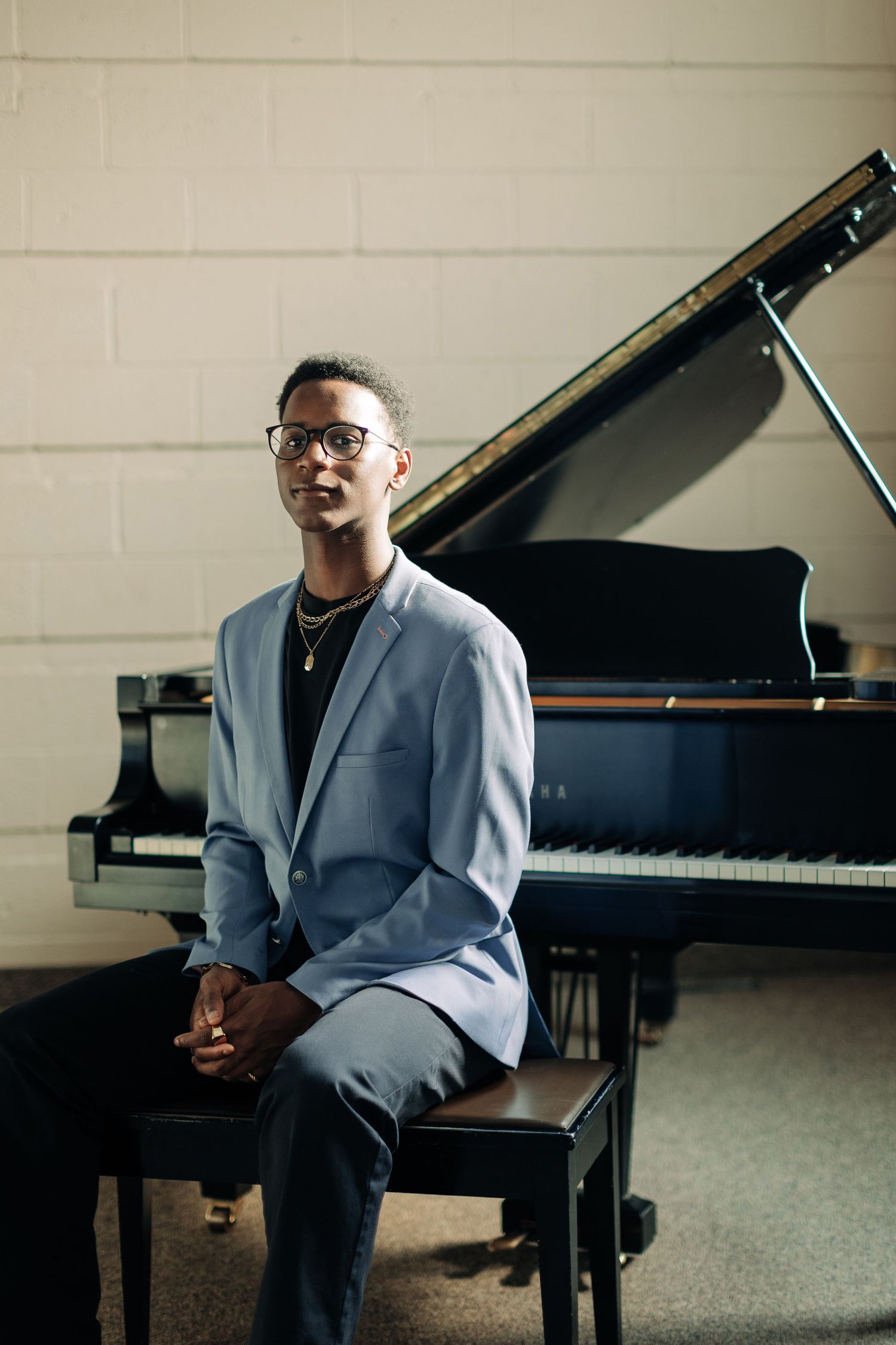 Professional pianist in grey blazer posed formally at grand piano.