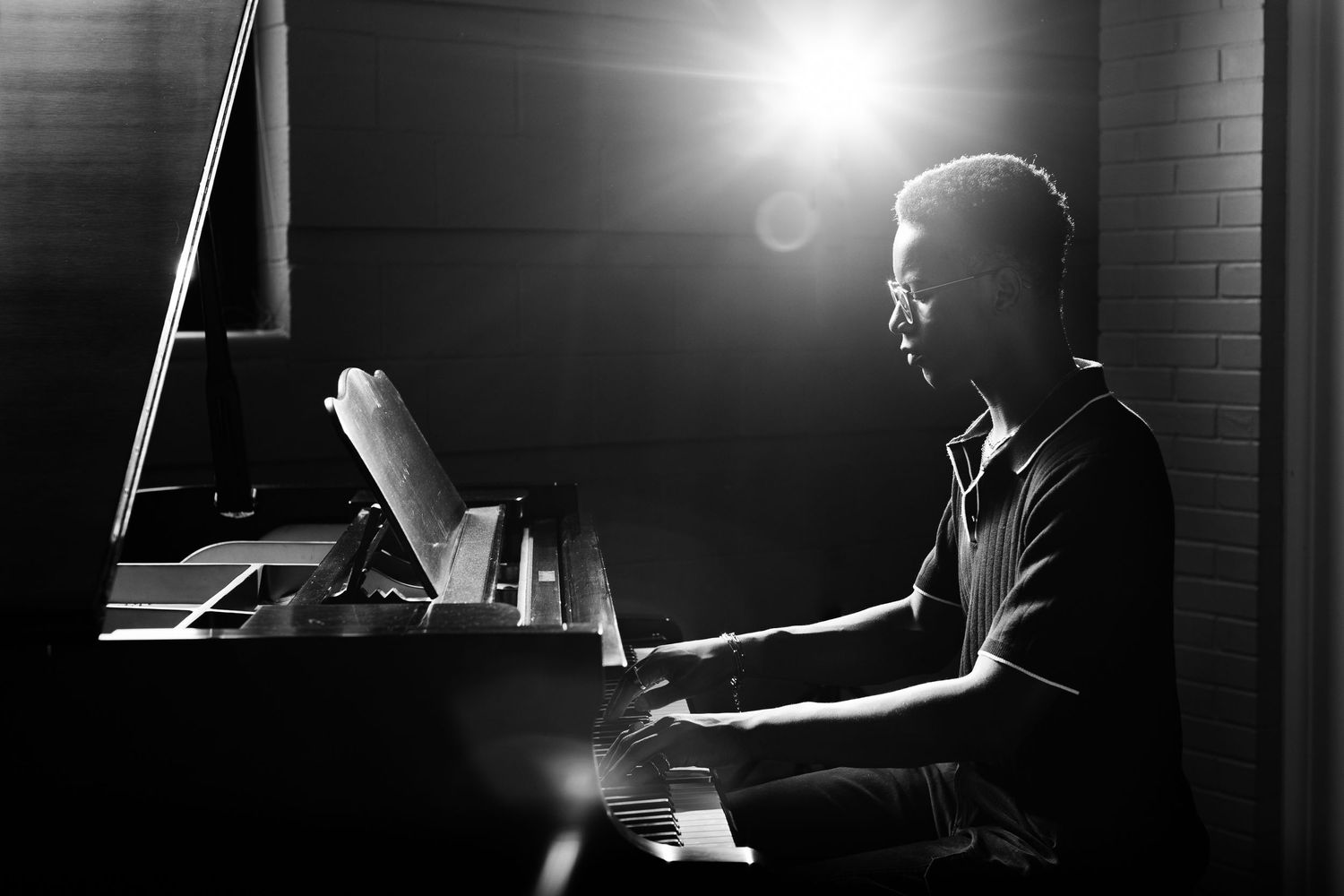 Pianist performing in dramatic lighting at grand piano.