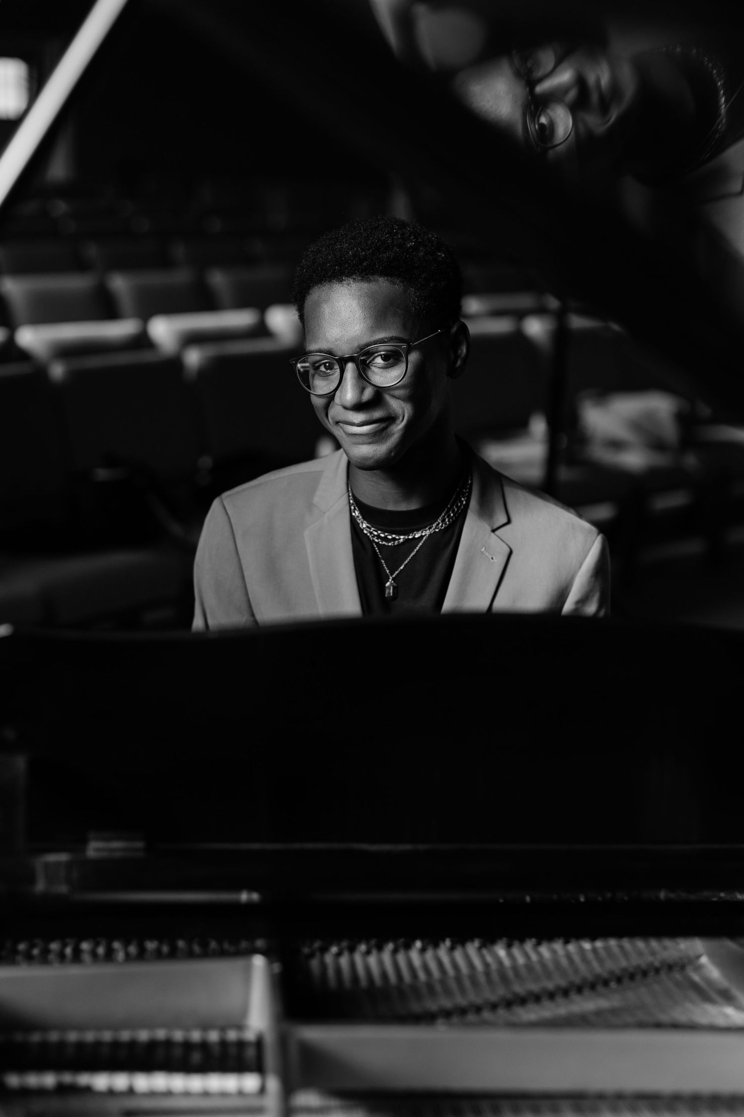 A pianist sits at a grand piano in formal attire, captured in black and white.