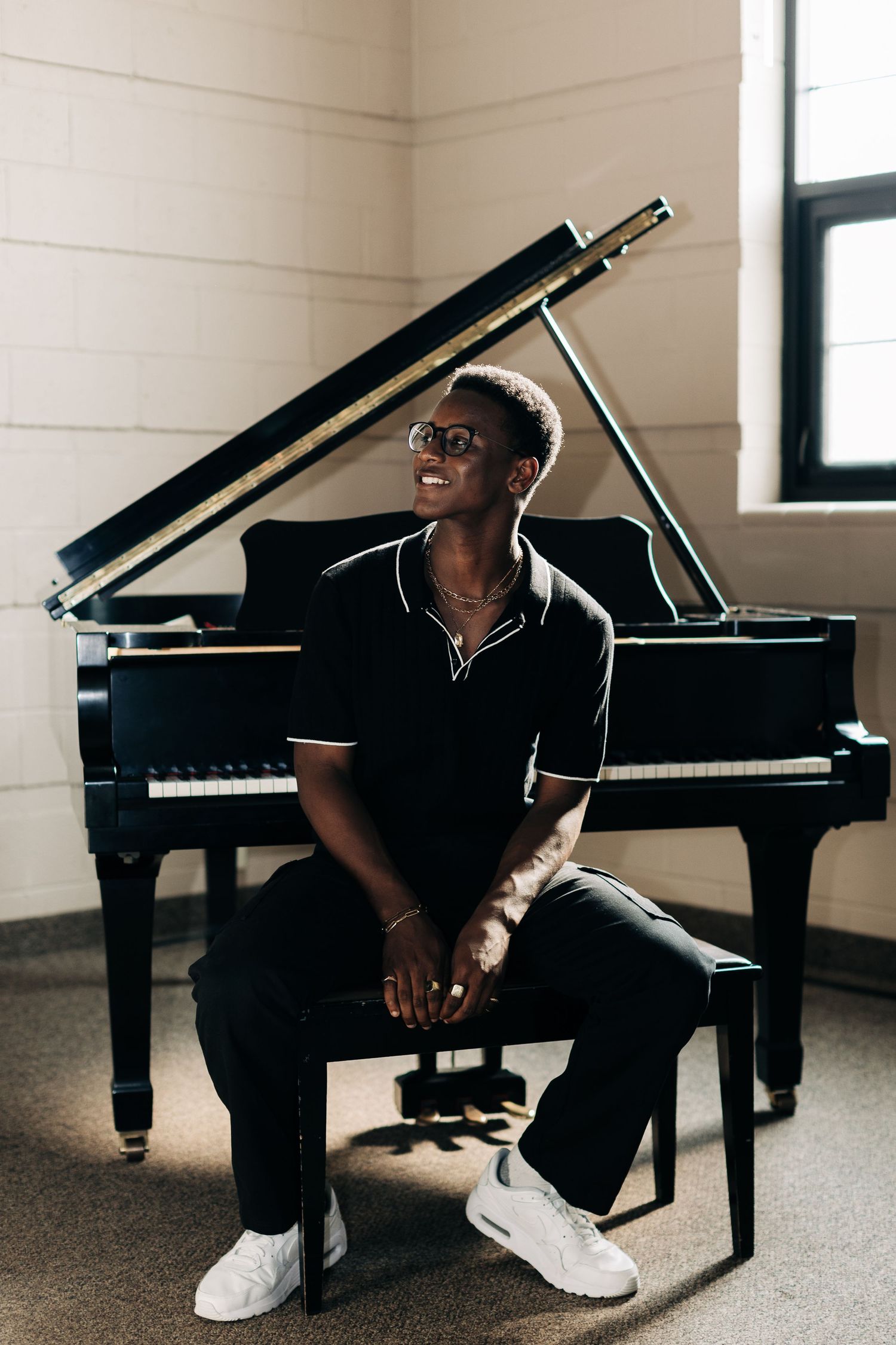 Musician in black outfit sitting at grand piano in bright studio space.