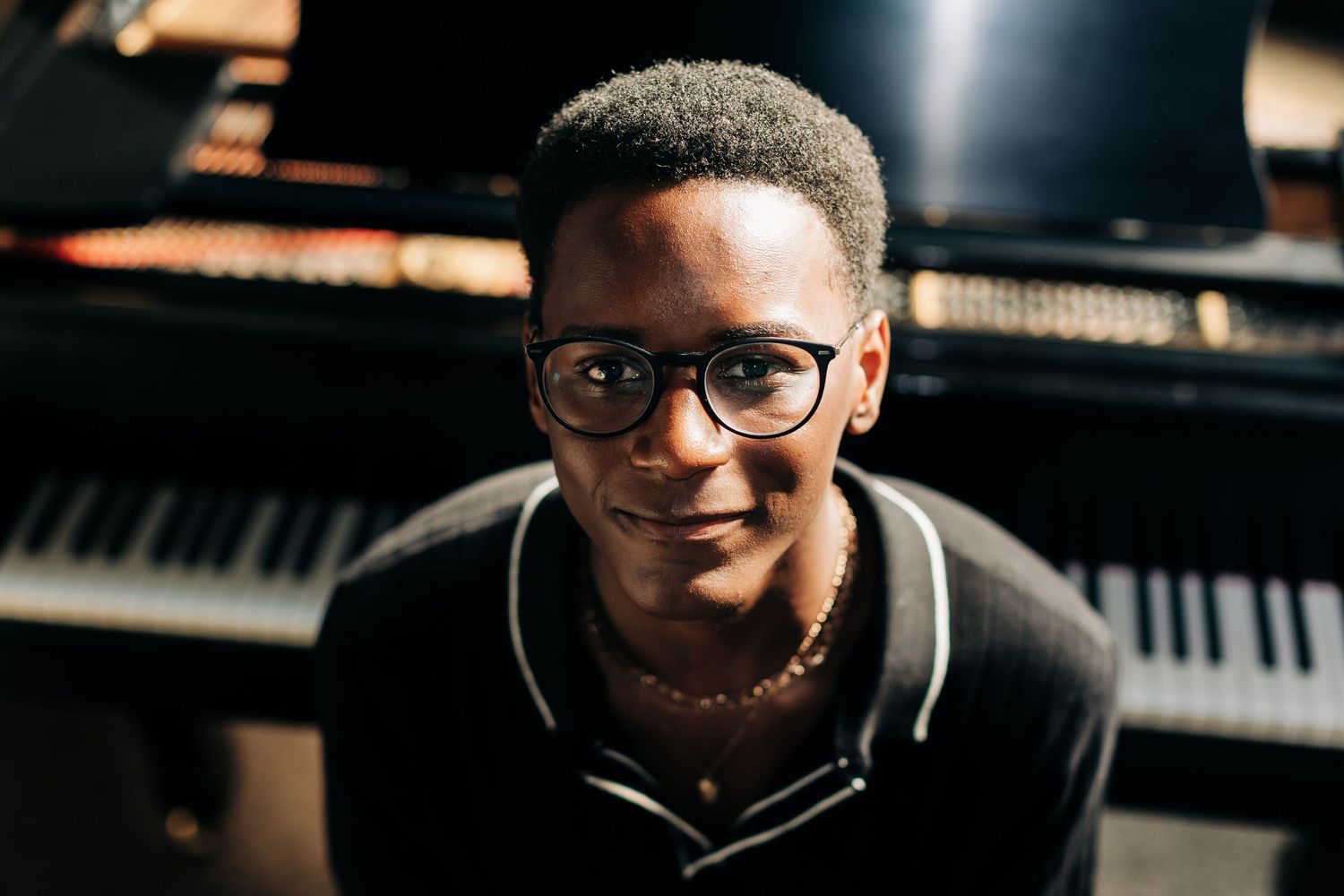 Portrait of pianist in glasses smiling at grand piano.