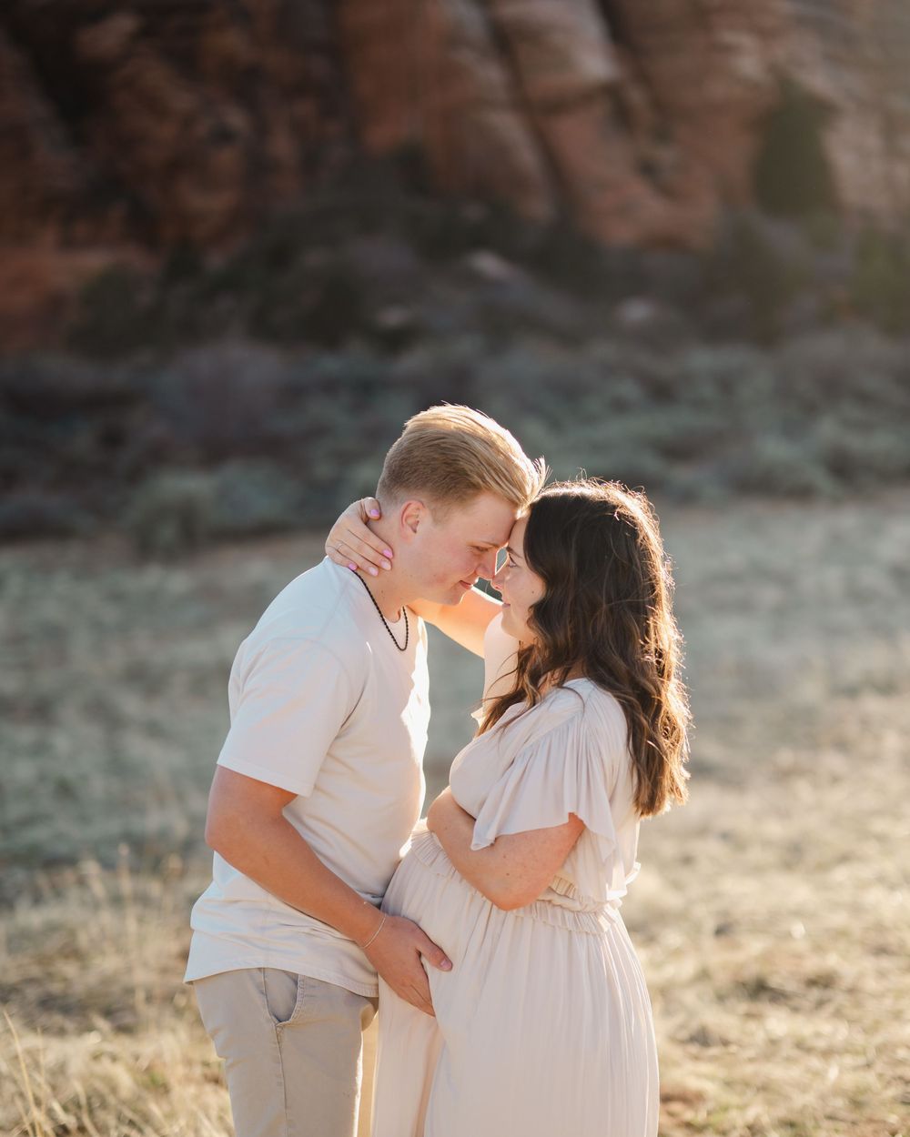 A romantic sunset photoshoot in nature with couple in light colored outfits embracing.