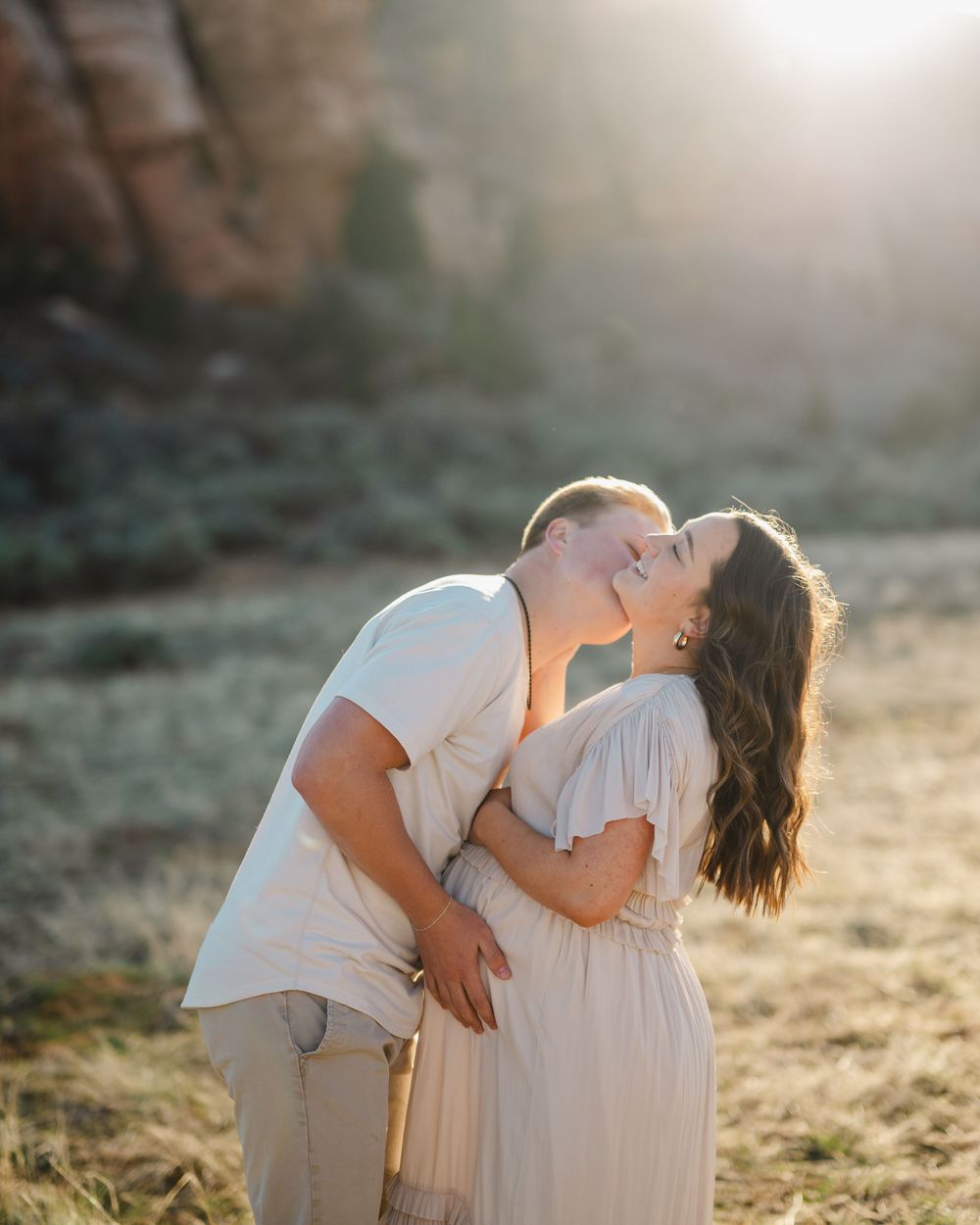 Tender embrace between couple in neutral clothing during sunset photoshoot.