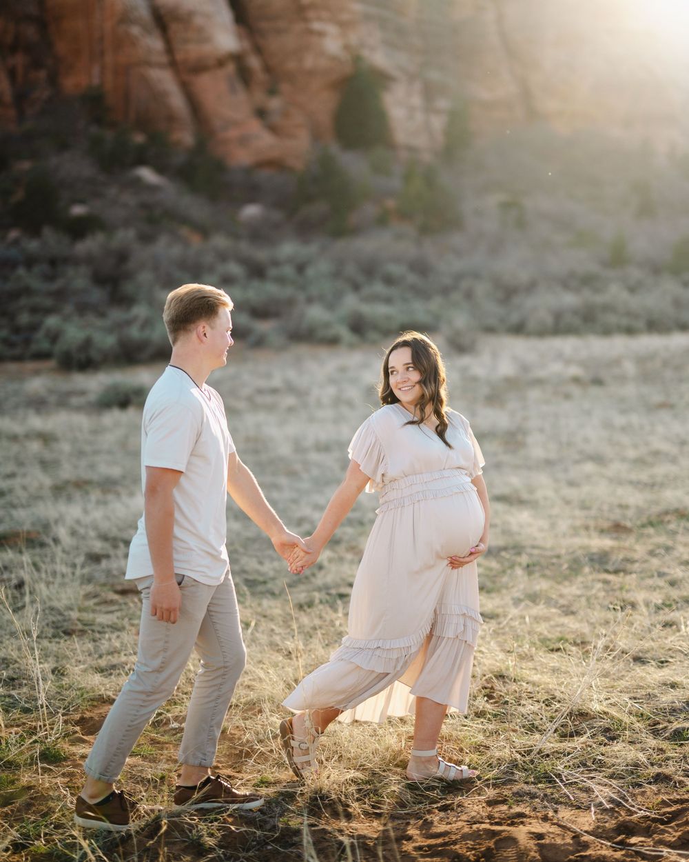 Maternity photoshoot in desert setting with couple in white and beige outfits.
