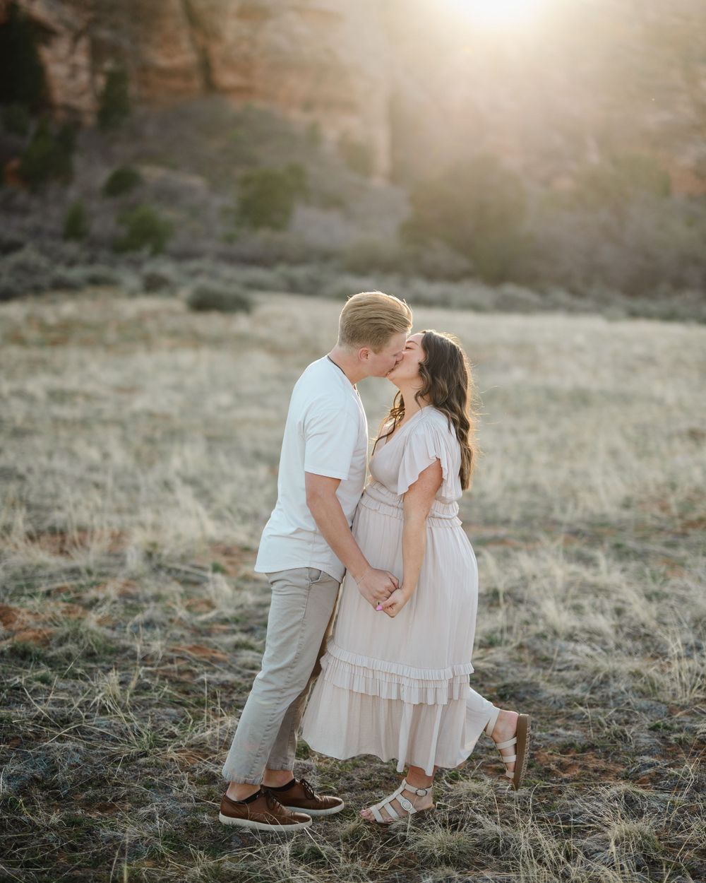 Romantic couple embracing during golden hour with dramatic desert cliffs in background.