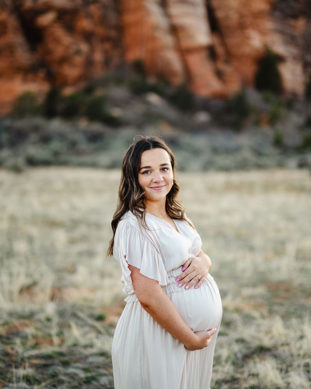 A maternity photo shoot in a scenic field with red rock formations in the background.
