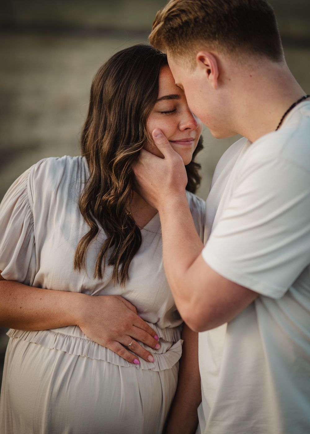 An intimate maternity photo shoot with a white dress against a dark background.