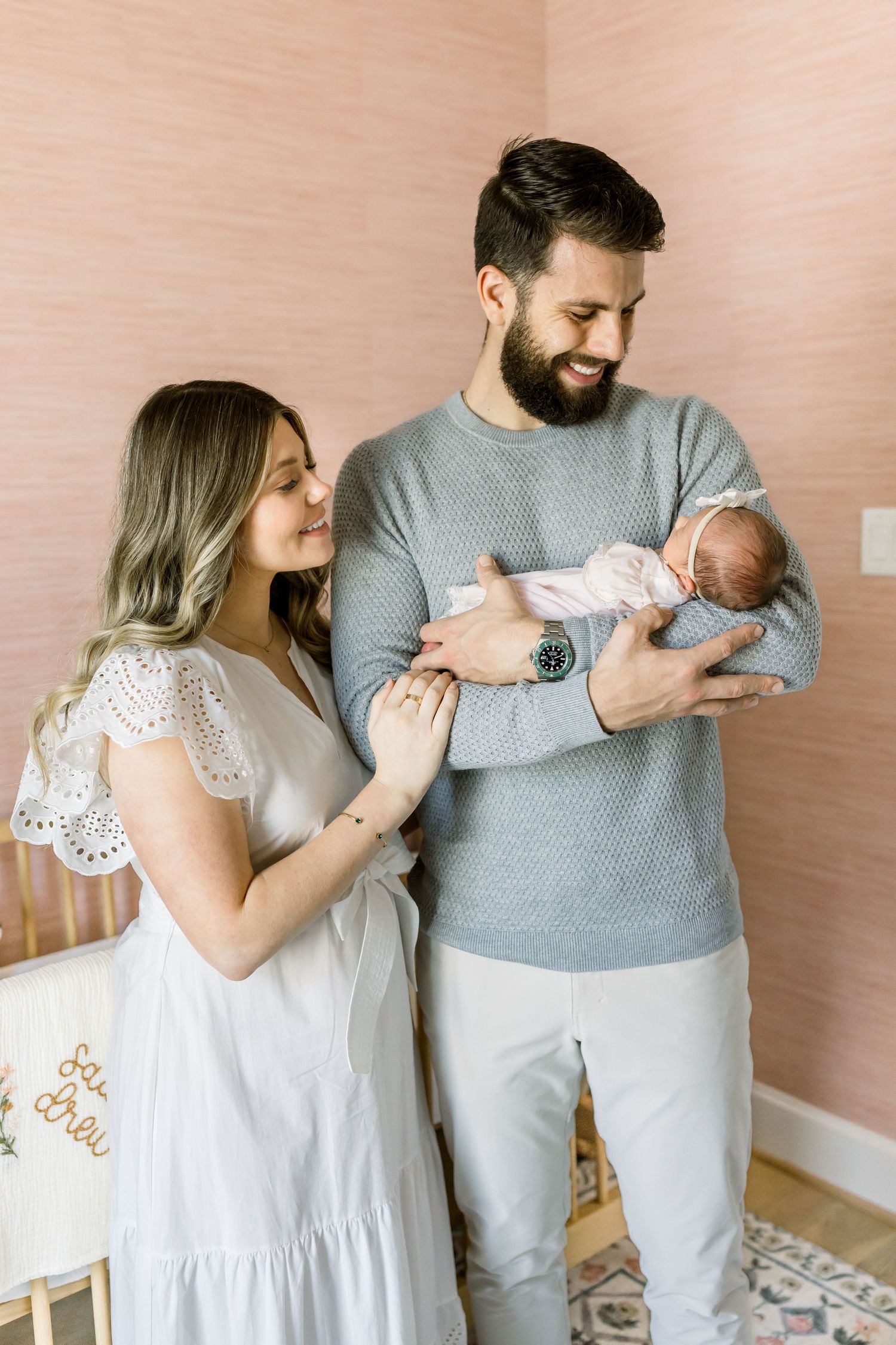 Parents share an intimate moment with their newborn baby in a pink-walled nursery.
