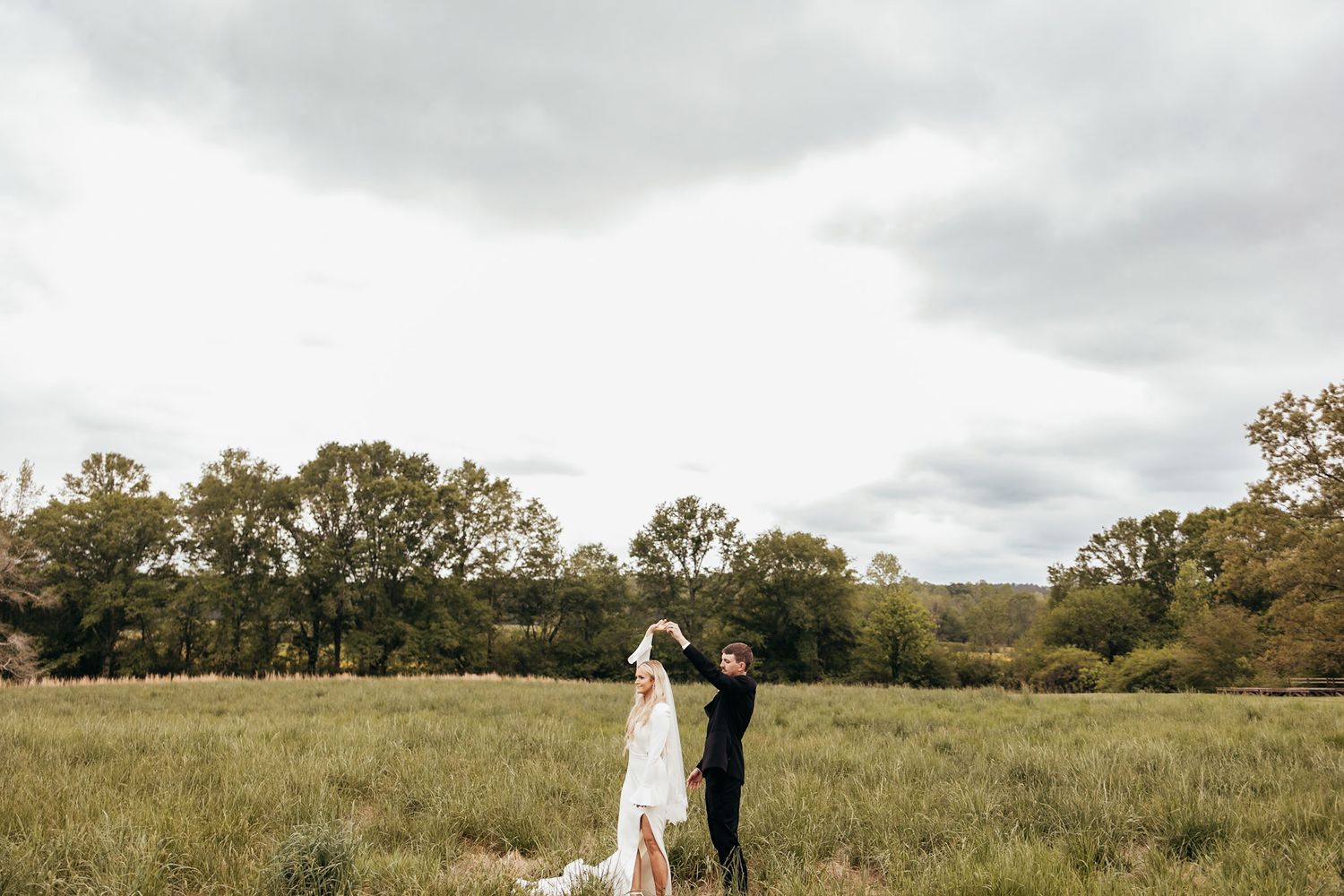 bride and groom dancing in a field before a thunderstorm
