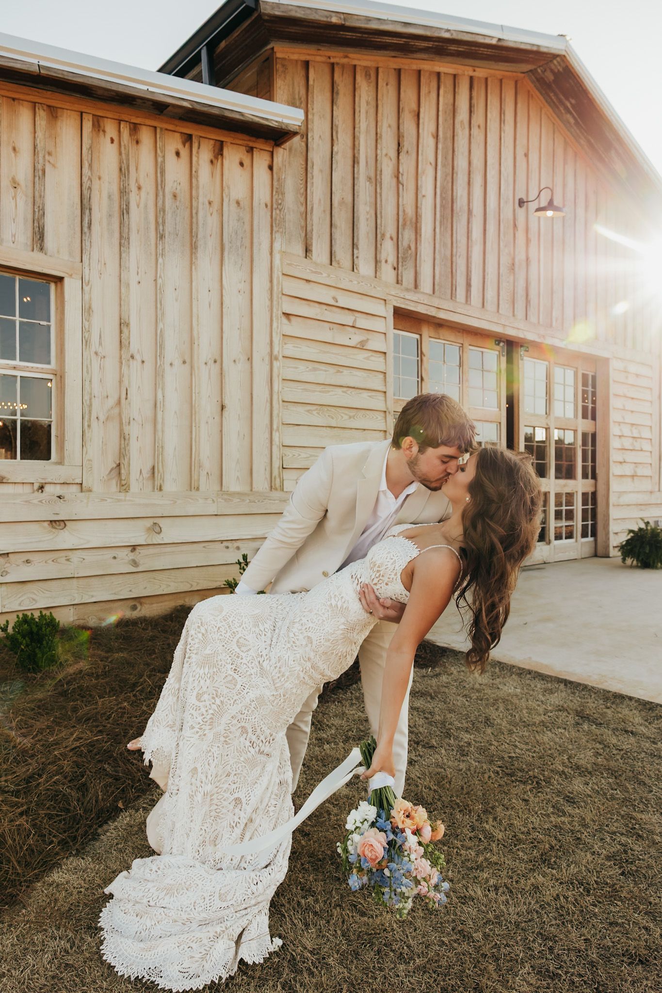 groom dipping and kissing bride in front of their barn venue