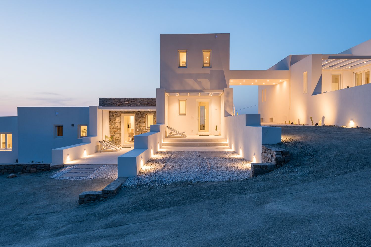 Illuminated white Mediterranean villa with stepped pathways and glowing windows at twilight.