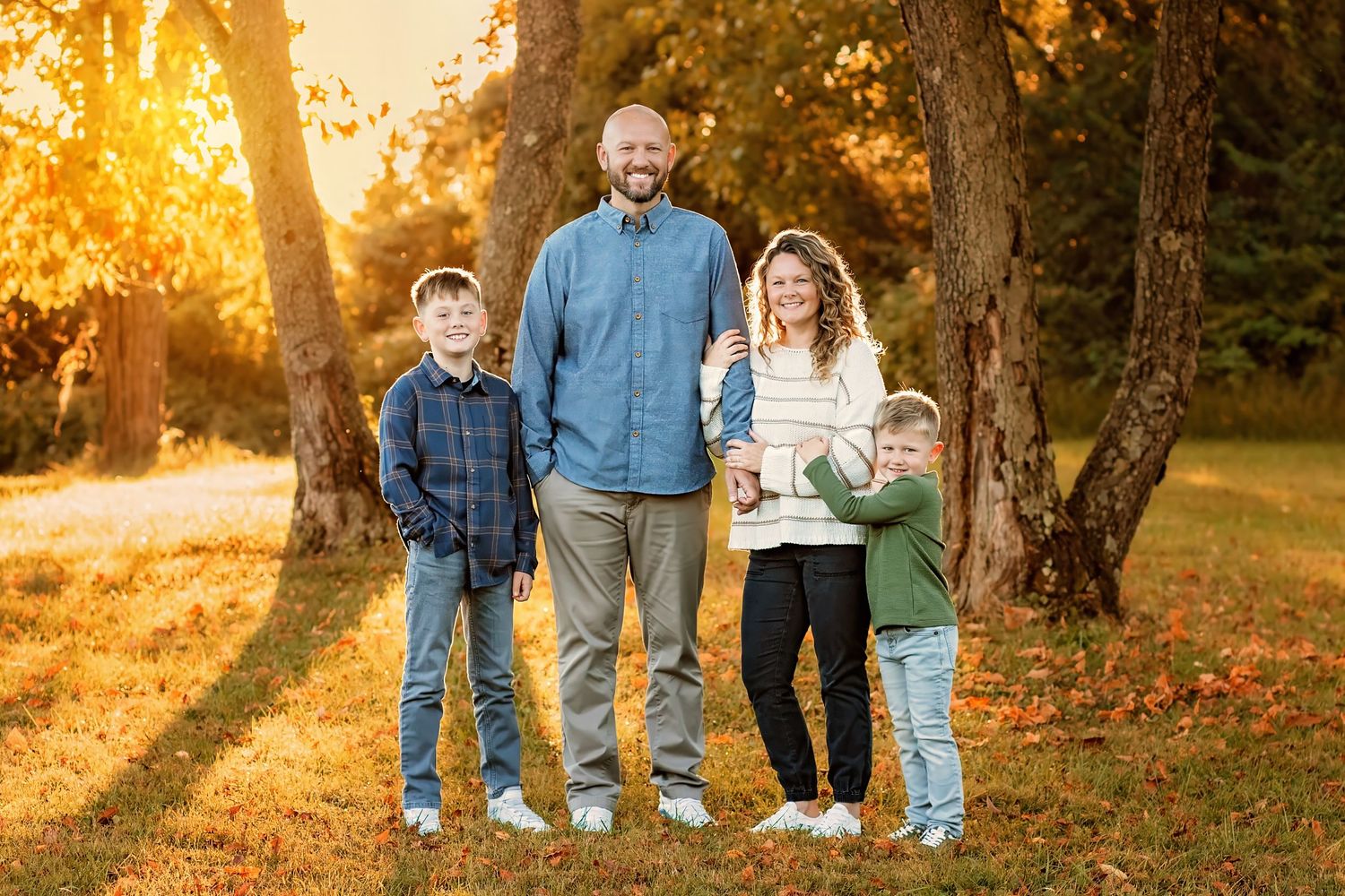 Happy family of four smiling together in golden autumn park with vibrant fall foliage at sunset.