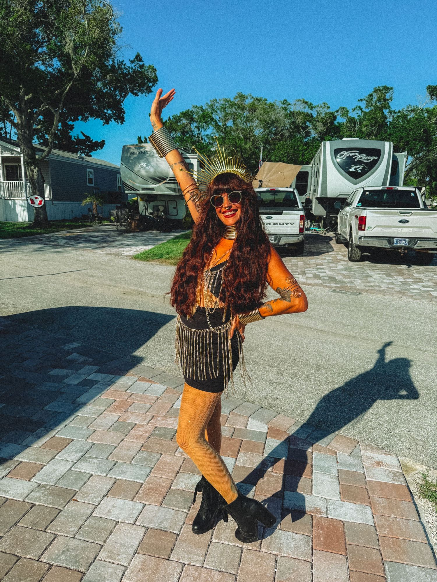 Woman in festival outfit with fringe skirt and hat posing near RVs on sunny day.