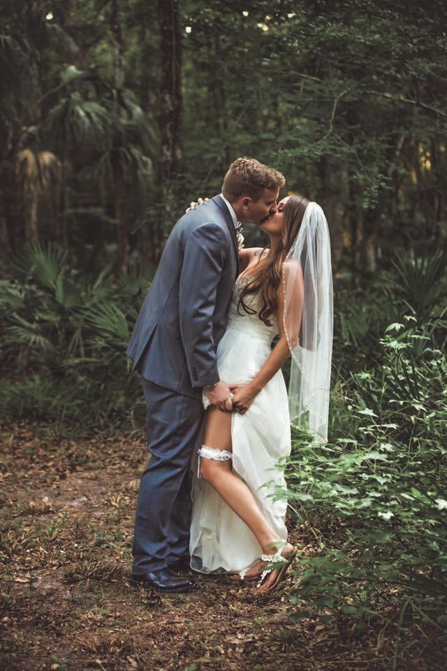 Romantic bride and groom sharing a kiss in a lush green forest during their outdoor wedding.