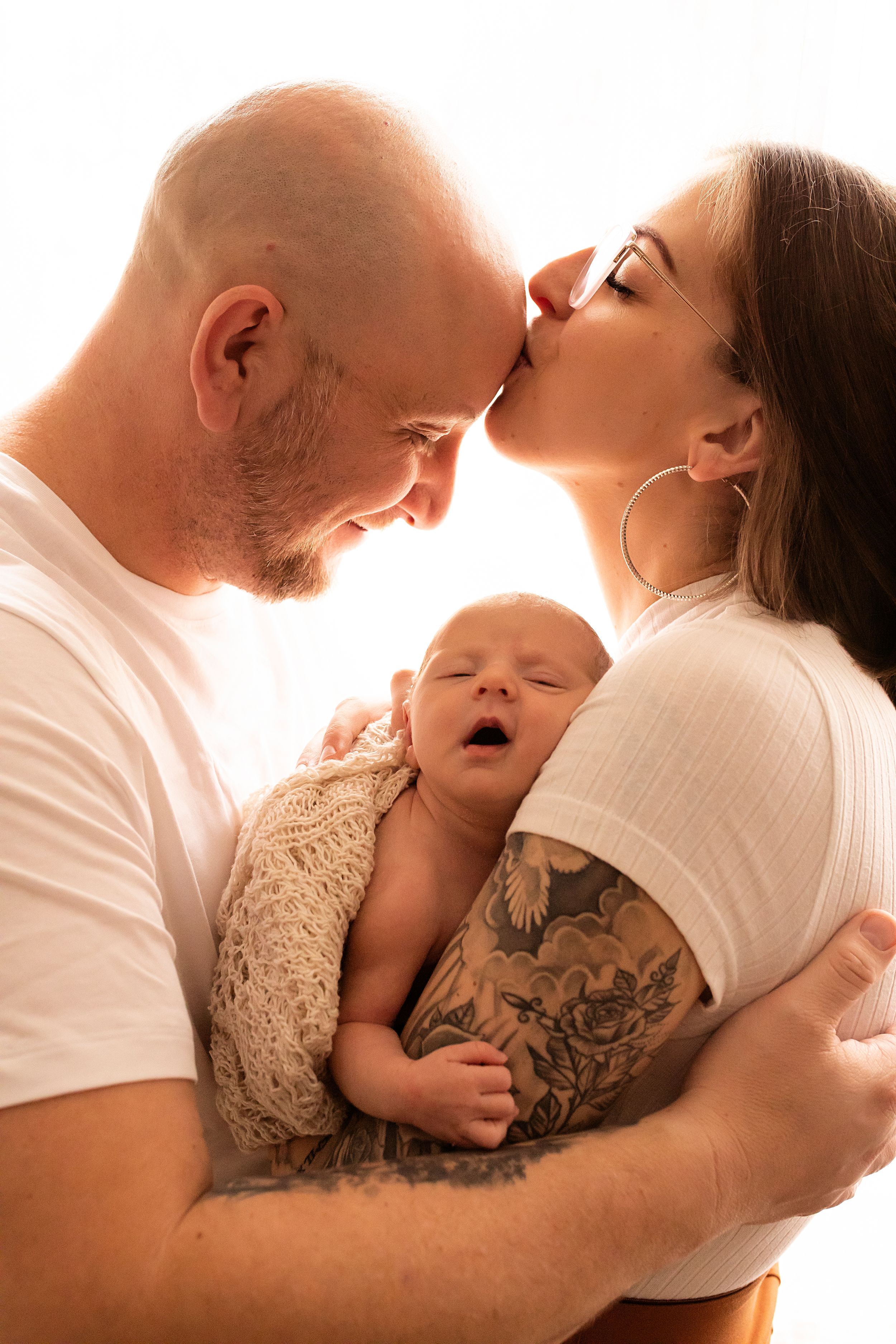 Intimate newborn photography session with parents in soft, warm lighting.