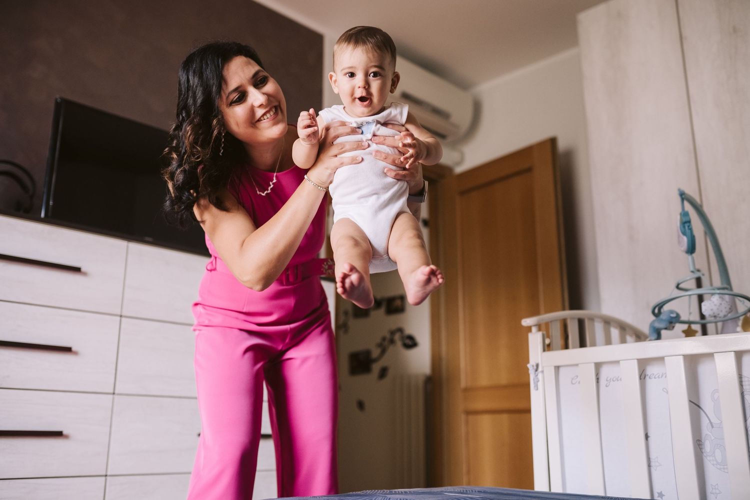 Mamma tiene tra le mani il suo bimbo facendolo volare per gioco sopra il letto e lui sembra divertirsi