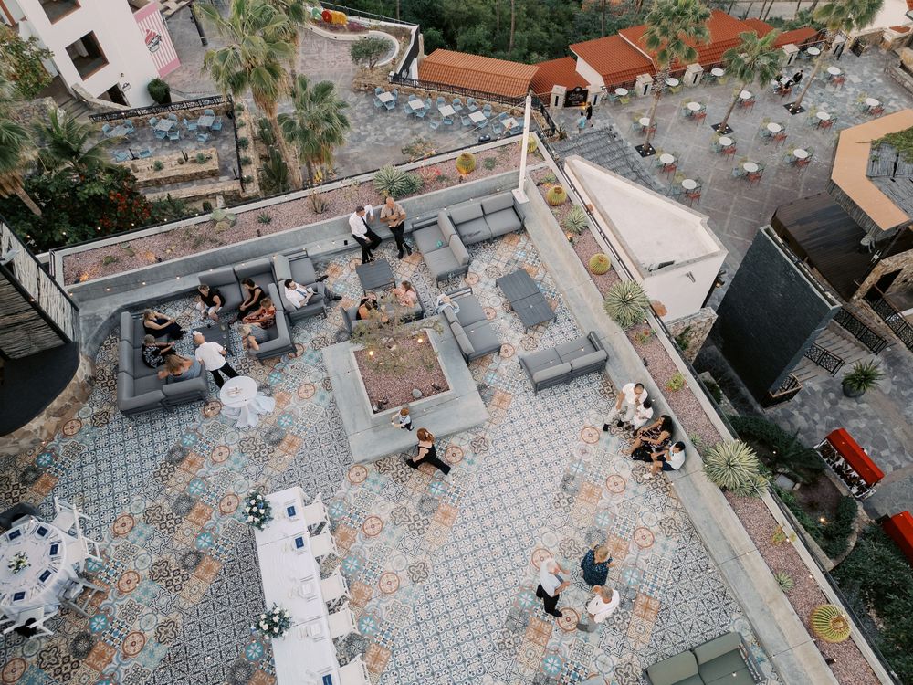 Aerial view of a paved plaza with tables and chairs arranged in a geometric pattern surrounded by buildings.