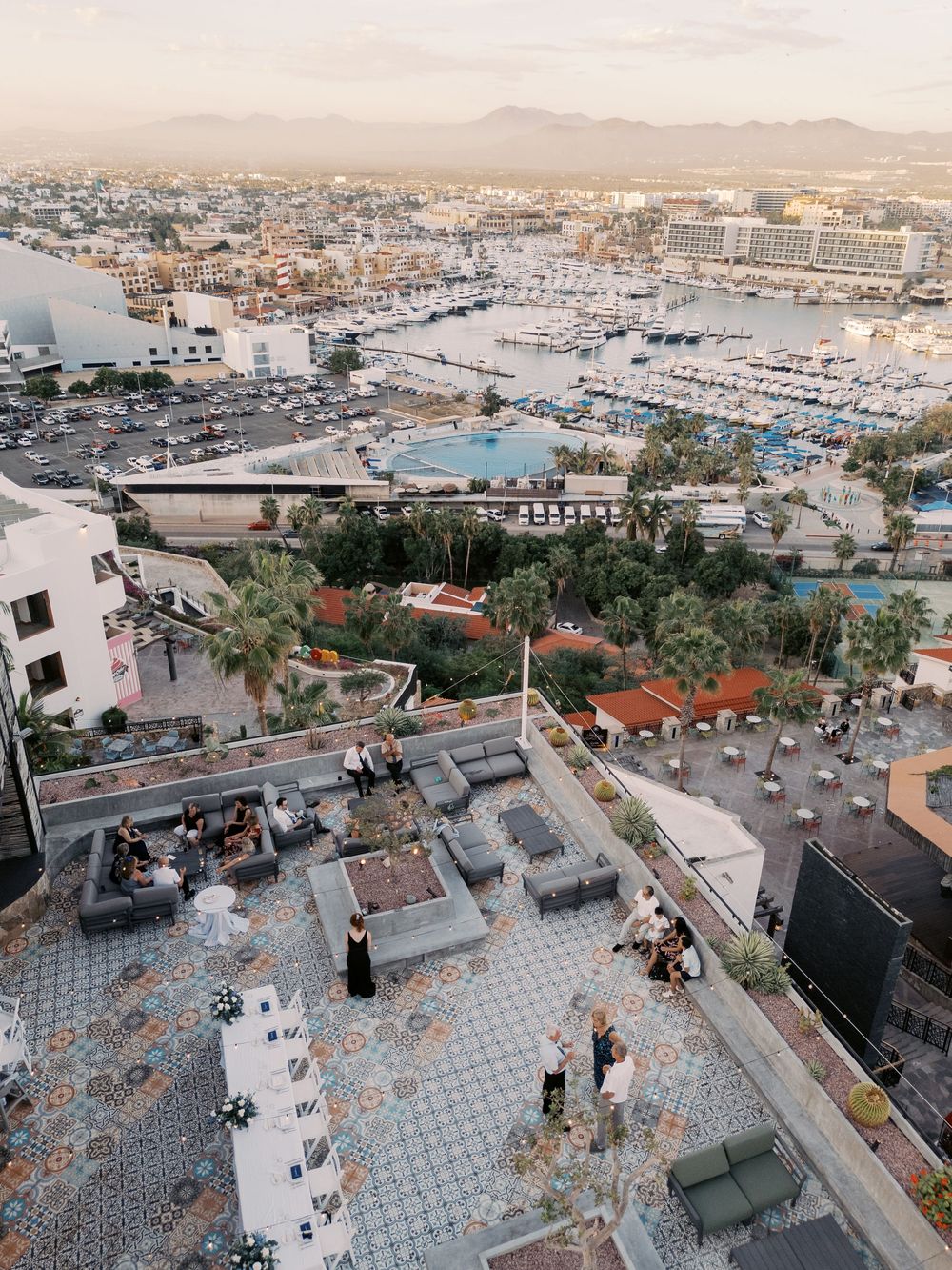 Aerial view of a coastal marina with boats docked in rows and mountains visible in the background at sunset.