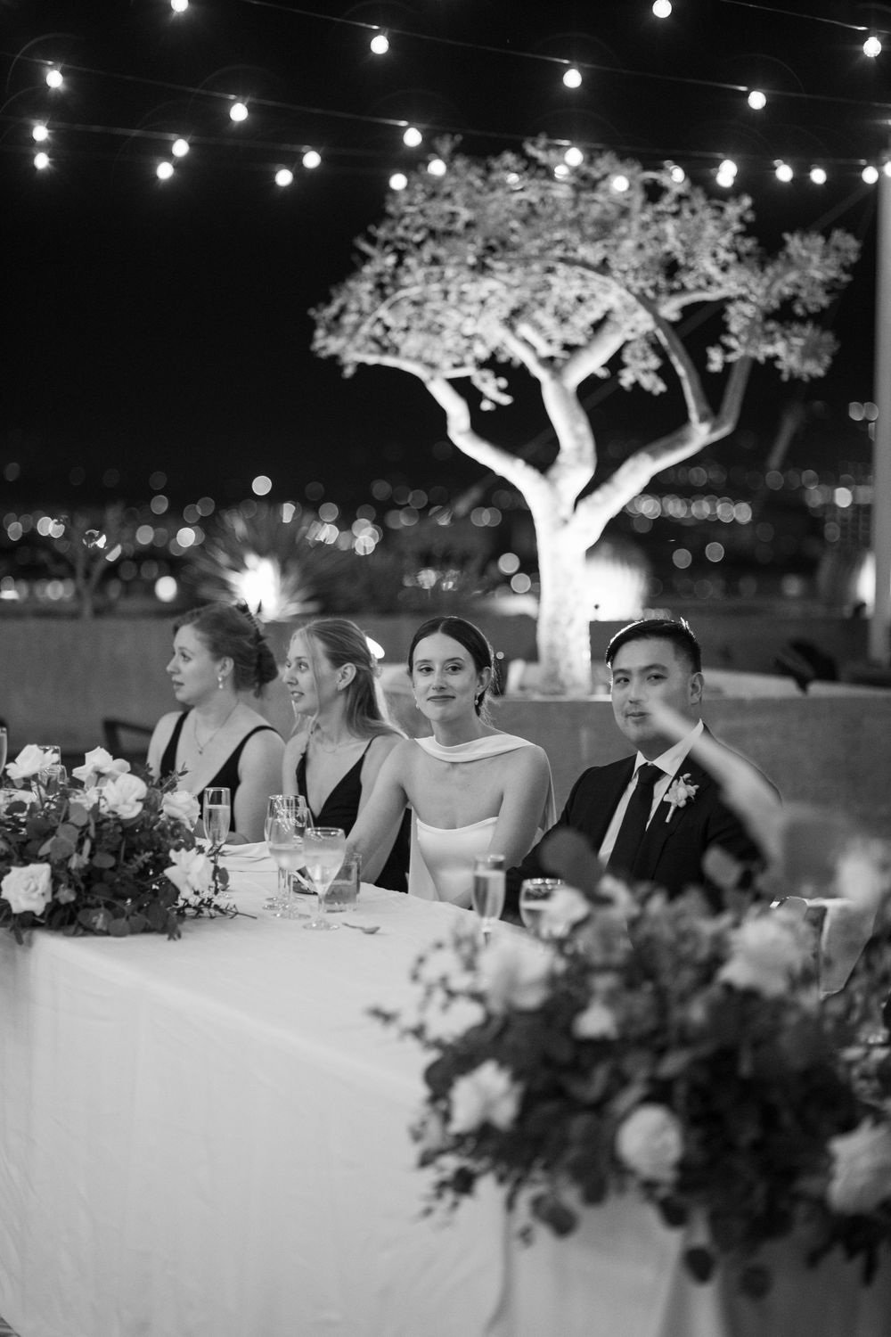 Wedding reception tables under string lights with floral centerpieces and illuminated trees.