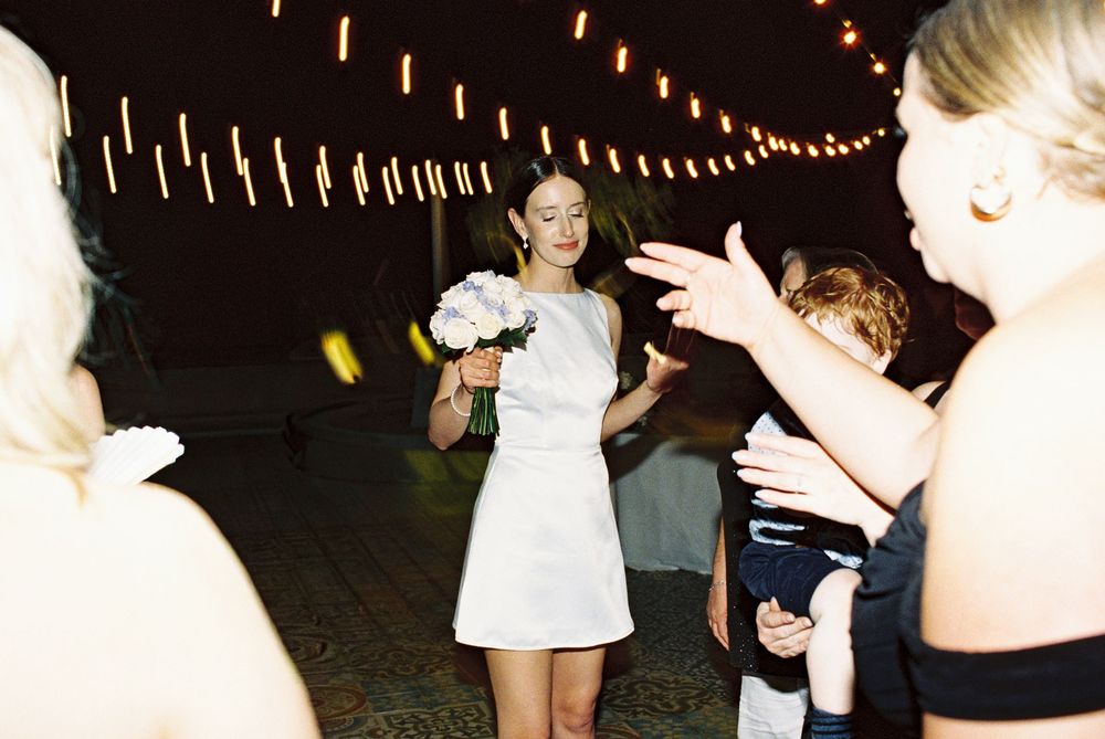 A person in a white dress smiles while dancing under string lights at an outdoor evening celebration.