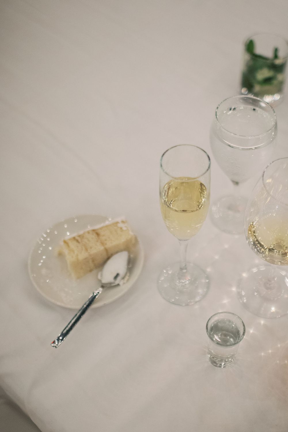 A slice of white wedding cake and champagne glasses arranged on an elegant white tablecloth.