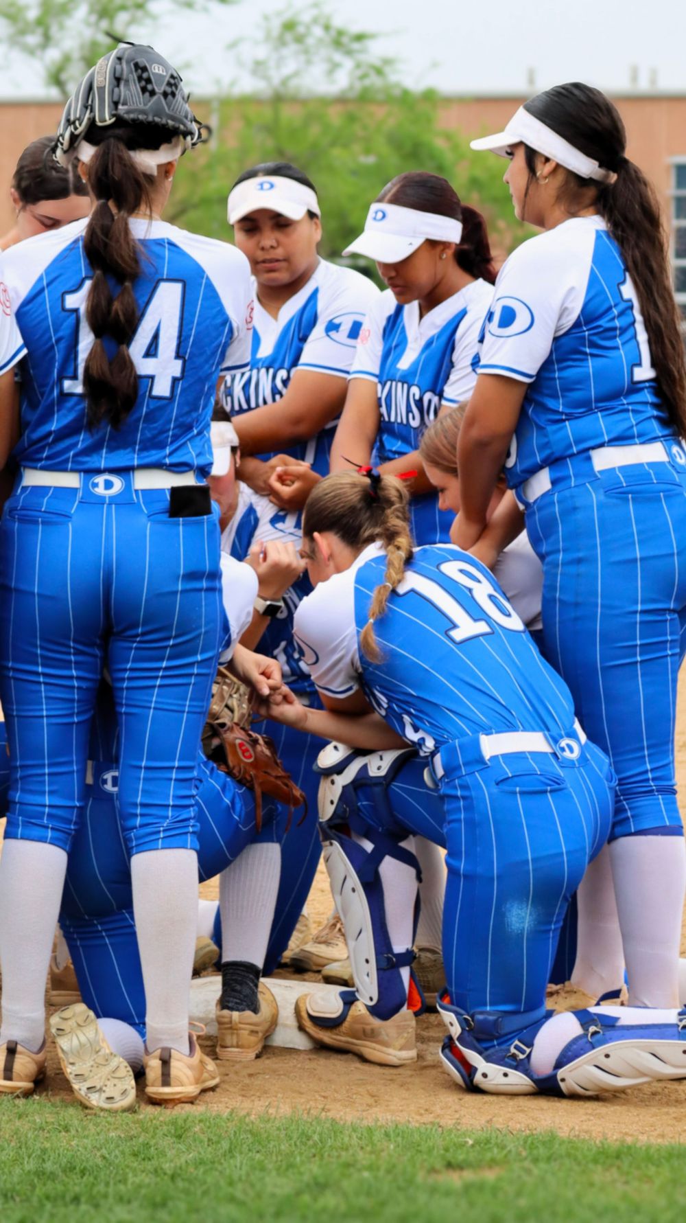 Softball team in blue uniforms huddles together on the field during a game.
