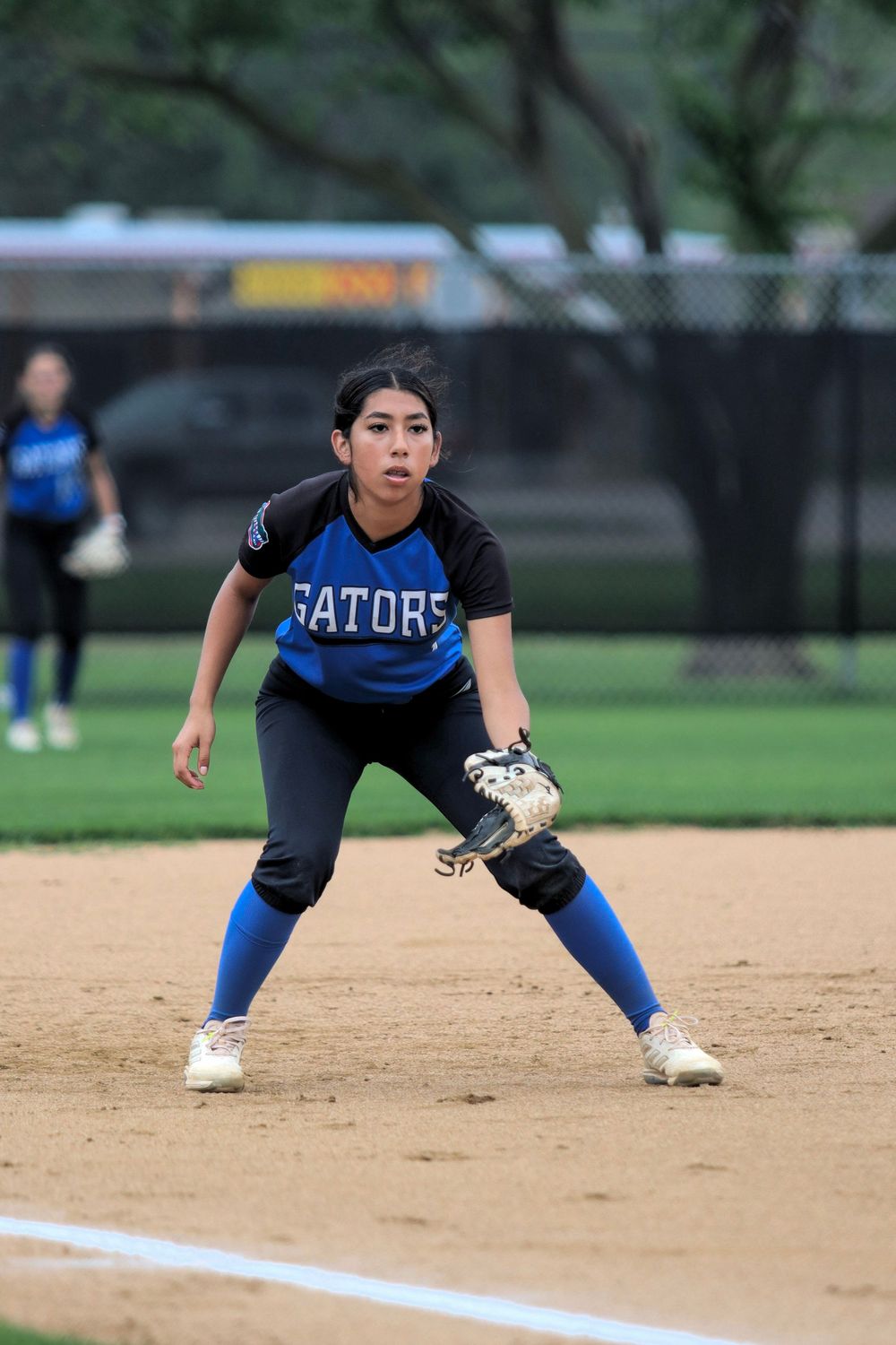 Softball infielder in blue Gators uniform takes defensive stance on the diamond.
