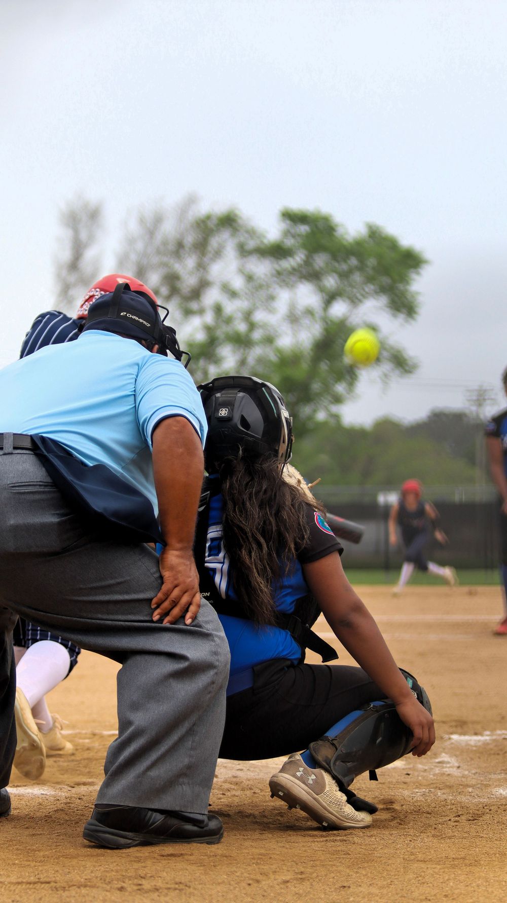 Softball catcher and umpire positioned behind home plate during game action.