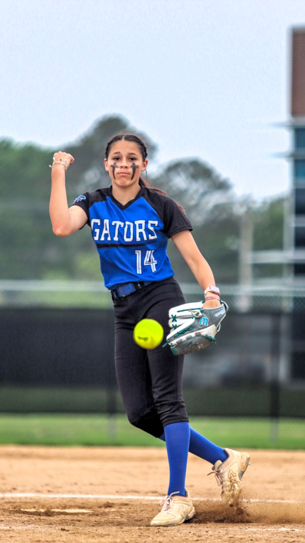 Softball player in Gators uniform pitching with dynamic windmill motion.