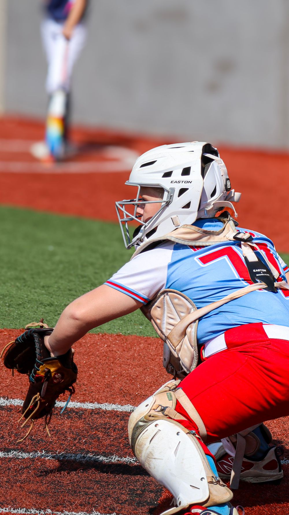 Softball catcher in protective gear diving to make a play during game.