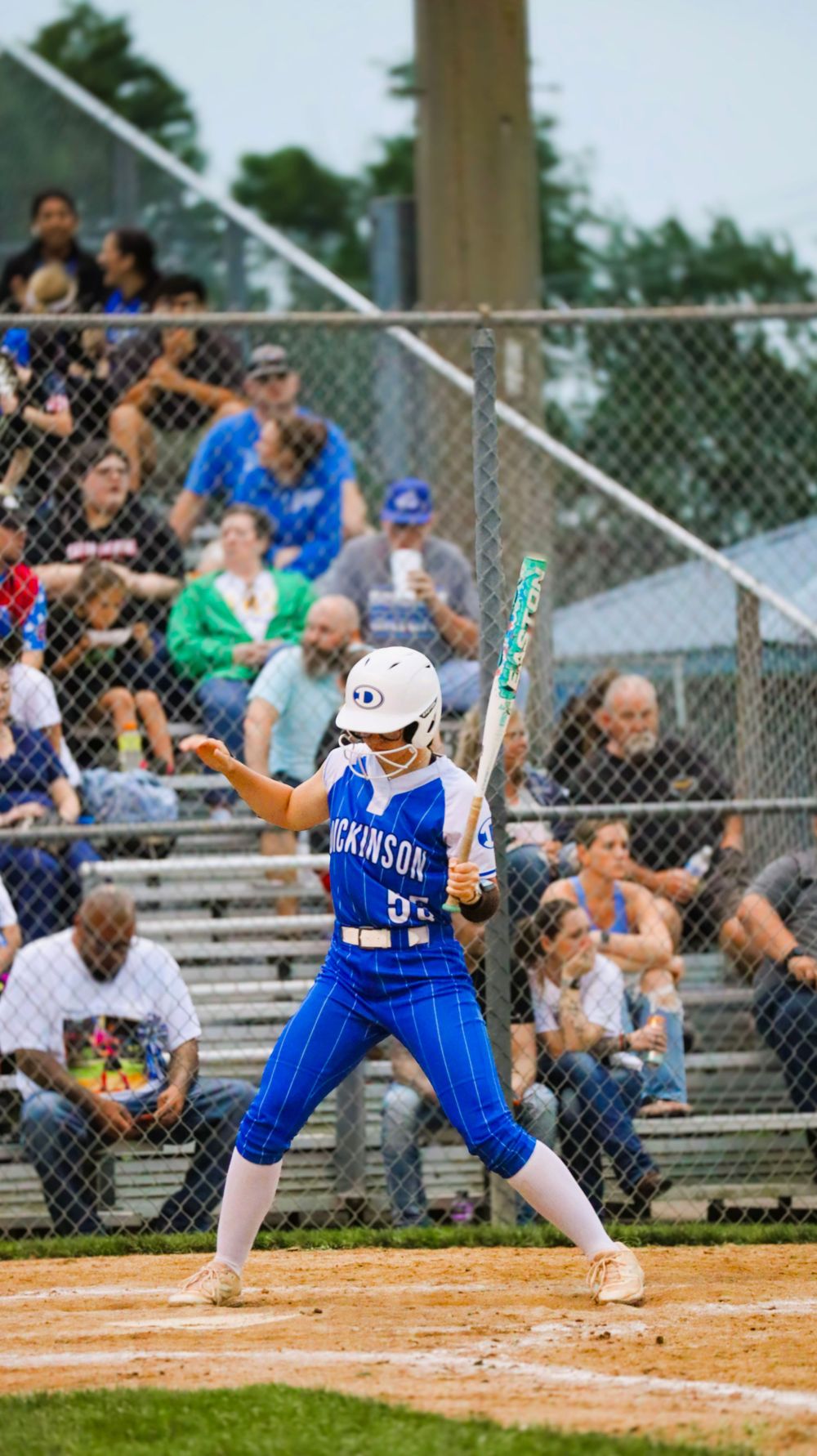 Softball player in blue uniform executes sliding technique at home plate during competitive game.