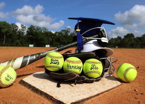 Softball equipment including yellow balls and bat arranged around home plate on dirt field.