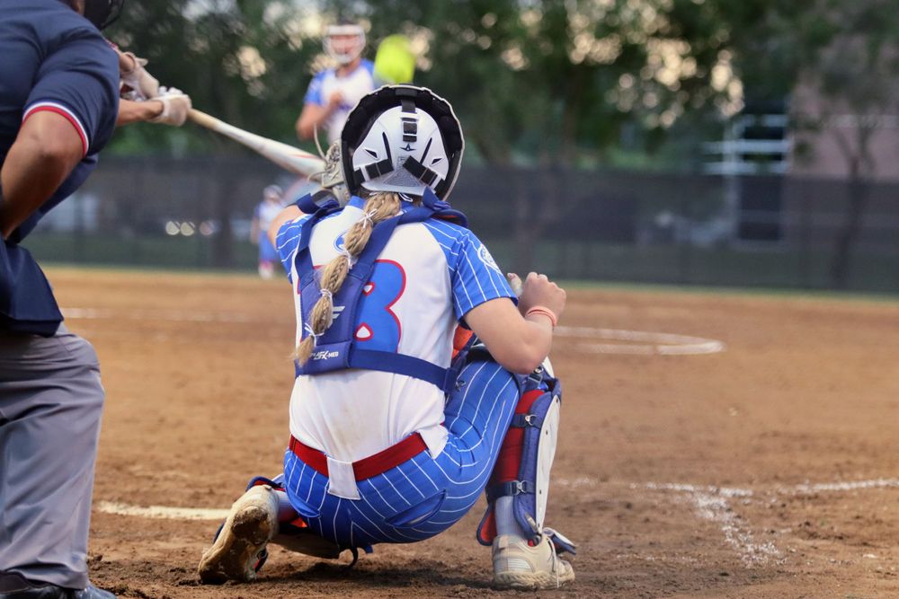 Youth softball players in action during competitive game on dirt field.