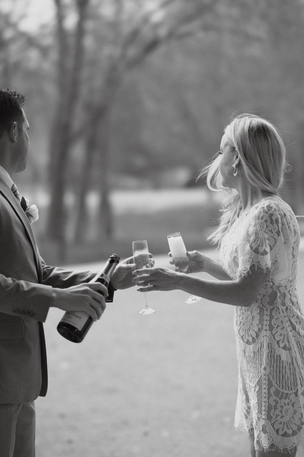 A couple sharing champagne outdoors in formal attire.