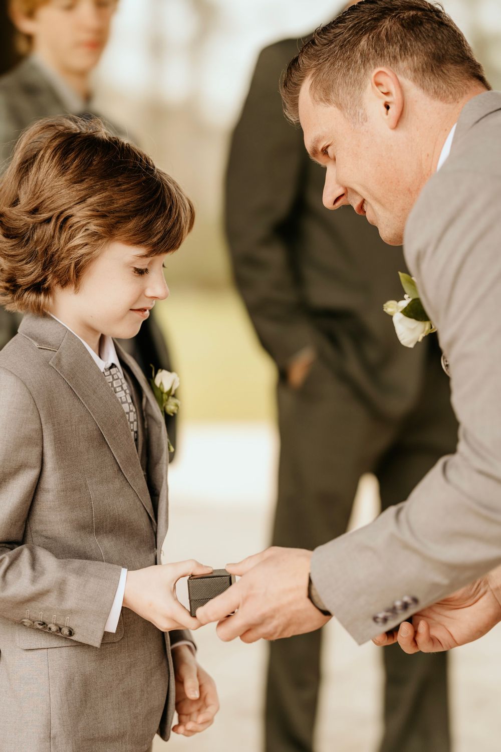 Touching moment during wedding ceremony as man presents ring to young boy in matching suit.
