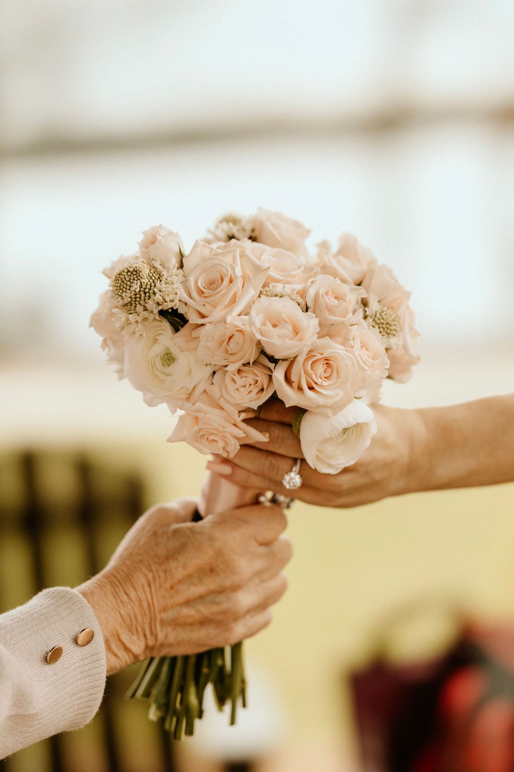 A delicate bouquet of blush pink roses being passed between hands.