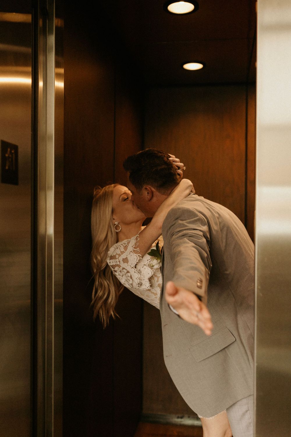 A romantic kiss shared in an elevator between a couple in formal wedding attire.