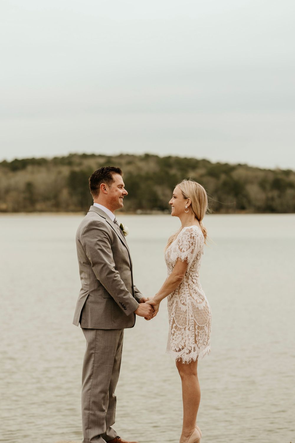 Newlyweds share a romantic moment while holding hands by the water.